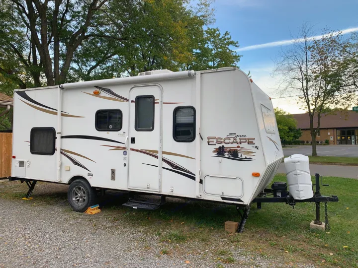 A white Spree Escape travel trailer, ideal for an RV rental adventure. Parked on gravel with trees, ready for camping.. Escape Trailer Industries Escape 5.0ta 2013