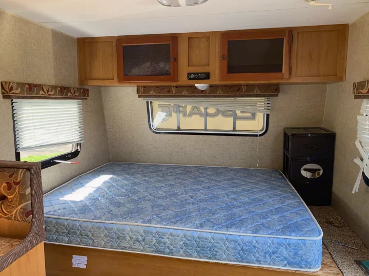 RV rental interior: A bedroom area with a blue patterned mattress, wooden overhead cabinets, and a window with blinds.. Escape Trailer Industries Escape 5.0ta 2013
