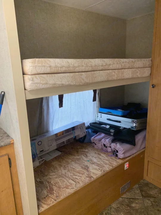 RV rental bunk beds: stacked mattresses on top, lower bunk transformed into organized storage for cases, a fan box, and purple bags.. Escape Trailer Industries Escape 5.0ta 2013