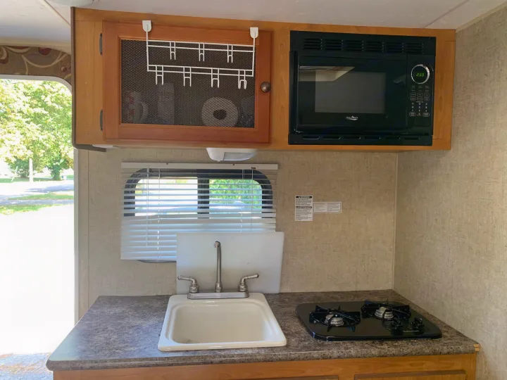 RV rental kitchen: compact area with a sink, two-burner stove, microwave, and mesh-front cabinet.. Escape Trailer Industries Escape 5.0ta 2013