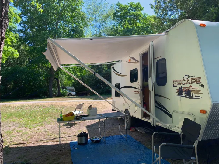 Enjoying the outdoors with an RV rental! This travel trailer has an extended awning, a table, and outdoor cooking setup at a sunny campsite.. Escape Trailer Industries Escape 5.0ta 2013
