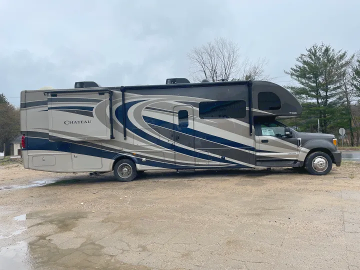A "RENT ME!" Chateau RV rental is parked on a wet lot under an overcast sky, ready for your next adventure.. Thor Chateau 2018