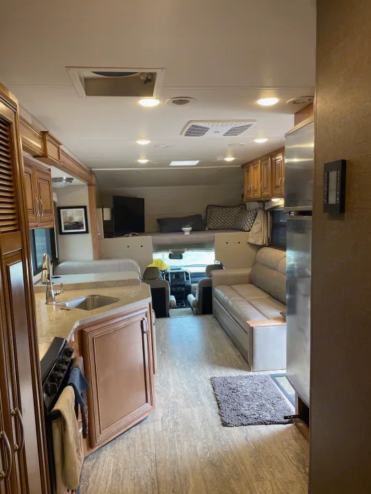 Inside a cozy RV rental: kitchen counter, sink, stove, couch, and cab-over bed. Ideal camper living space.. Thor Chateau 2018