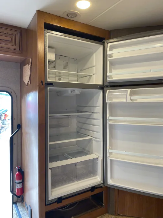 Clean, empty two-door refrigerator in an RV rental, ready for use. Features visible shelves, drawers, and freezer.. Thor Chateau 2018