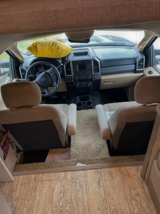 RV rental cockpit view: Ford Super Duty dashboard, beige front seats, and transition from shaggy carpet to laminate flooring.. Thor Chateau 2018