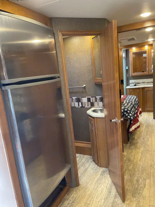 RV rental interior: stainless steel fridge, open door to bathroom sink, and bedroom with patriotic quilt.. Thor Chateau 2018
