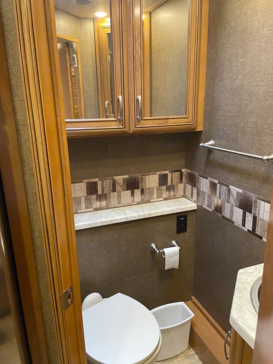 Interior of an RV rental bathroom, showcasing warm wood cabinets, a clean toilet, and decorative tile backsplash. Compact and practical.. Thor Chateau 2018
