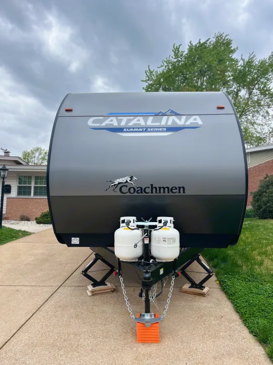 This Catalina Summit Series travel trailer, ideal for RV rental, is shown from the front with propane tanks and leveling blocks.. Coachmen Summit series 2023