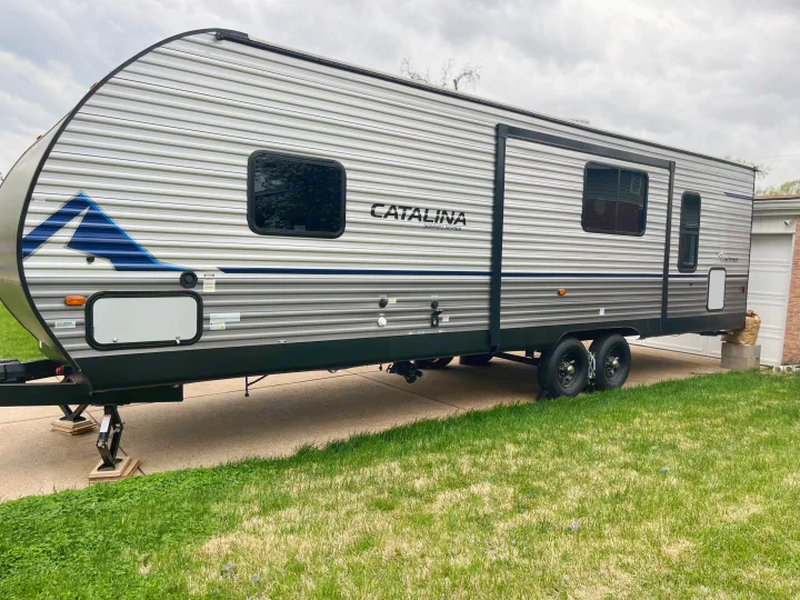 Side view of a gray Catalina Summit Series travel trailer, an ideal RV rental parked on a driveway.. Coachmen Summit series 2023