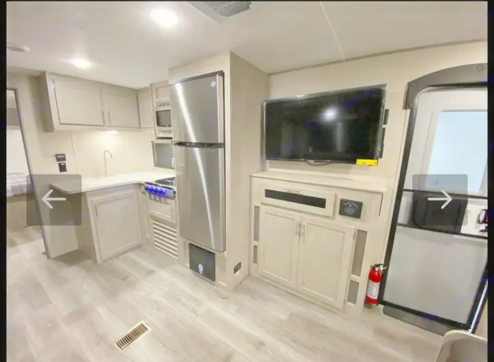 RV rental interior: modern kitchen with stainless appliances, TV entertainment center, and light wood flooring.. Coachmen Summit series 2023