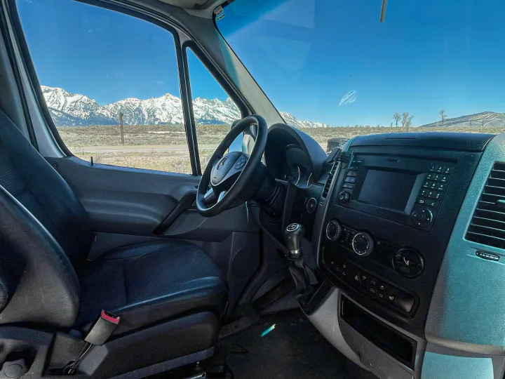 RV rental van interior with black seats & dashboard, offering a stunning view of snow-capped mountains for your next road trip.. Mercedes-Benz Sprinter 2016