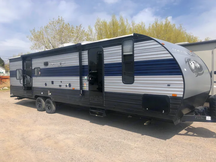 Grey and blue Grey Wolf travel trailer, ideal for an RV rental adventure. Parked on gravel, trees in background.. Forest River Cherokee Grey Wolf 2022