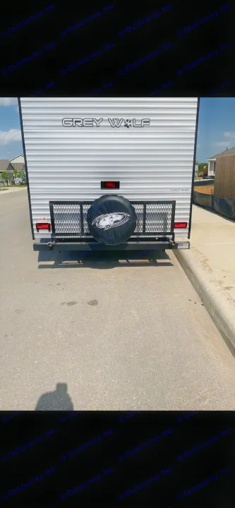 Rear view of a Grey Wolf travel trailer, an ideal RV rental with a spare tire & cargo rack, parked on asphalt.. Forest River Cherokee Grey Wolf Special Edition 2022