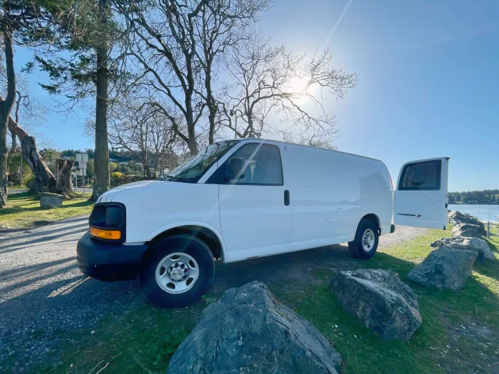 White cargo van, ideal for RV rental conversion, parked by sunny waterside with trees and rocks.. Chevrolet Other 2009