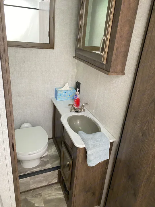 Compact RV rental bathroom with toilet, sink, and vanity. Ideal for camping and travel trailer adventures.. Gulf Stream Conquest 6280LE 2023