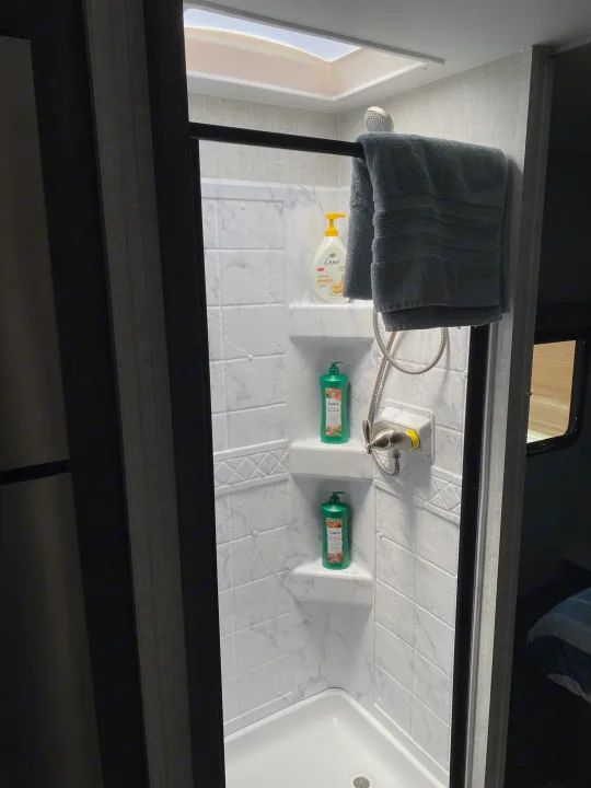 Spacious and clean RV rental shower features a skylight, fresh towel, and toiletries for a refreshing experience.. Gulf Stream Conquest 6280LE 2023