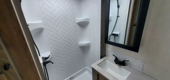 Modern RV rental bathroom featuring a white shower with herringbone pattern, sink, and black faucet.. Forest River Surveyor Legend 2022
