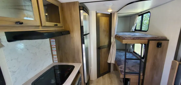RV rental: Interior view of compact kitchen with stove, fridge & marble-look backsplash, leading to cozy bunk beds.. Forest River Surveyor Legend 2022