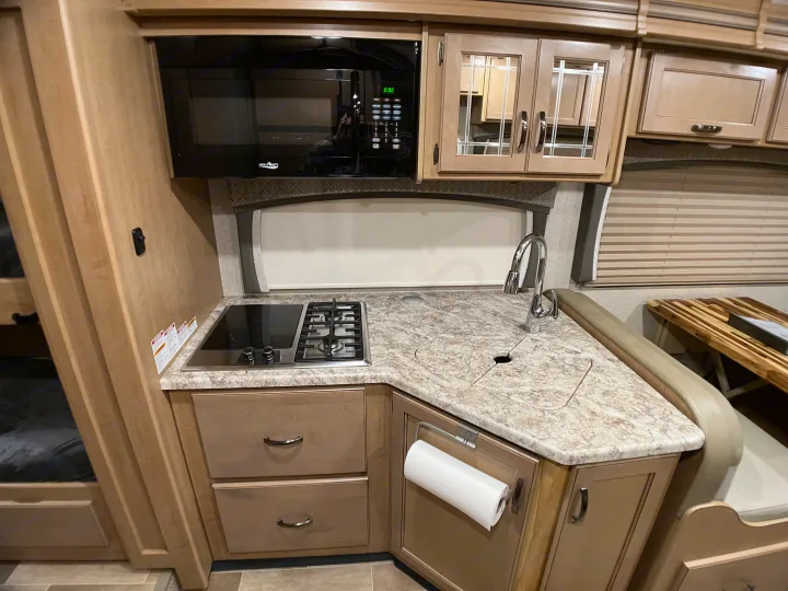 Modern RV rental kitchen featuring a microwave, built-in cooktop, sink, and light wood cabinetry.. Thor Chateau 2020