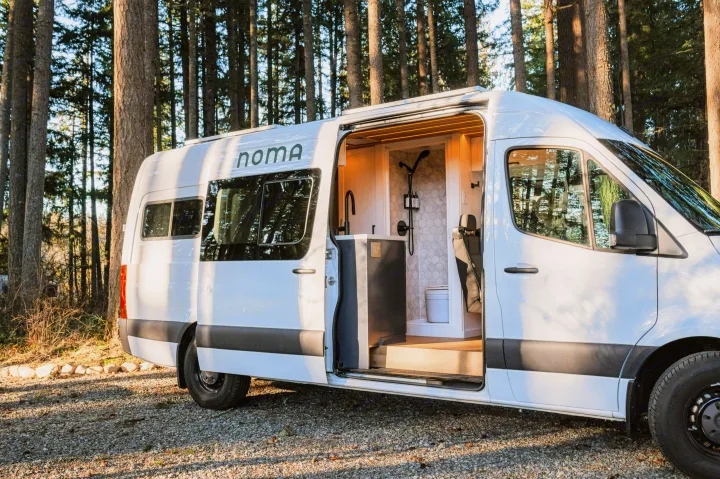 Noma rv rental parked among trees, showcasing a modern camper van interior with a sleek kitchen and shower area.. Mercedes-Benz Sprinter 2021