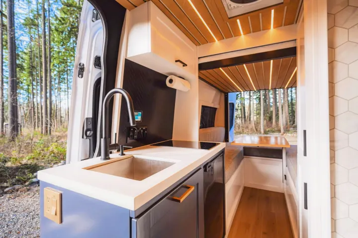 Inside a stylish rv rental: a well-equipped kitchen, comfortable dining space, and serene forest backdrop.. Mercedes-Benz Sprinter 2021