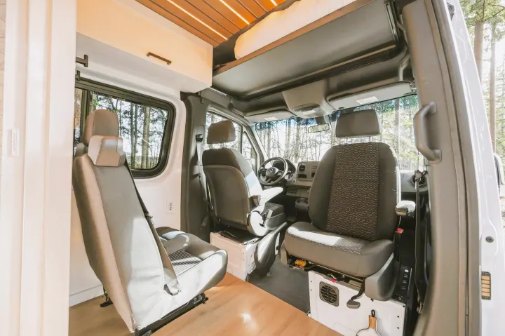 Interior of an RV rental camper van, showing the front seats, dashboard, and custom overhead storage with a slatted ceiling.. Mercedes-Benz Sprinter 2021