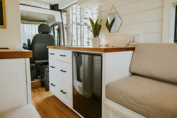 RV rental interior features a compact kitchen, cozy seating area with nature views, and modern finishes.. Ram Promaster 2500 2019