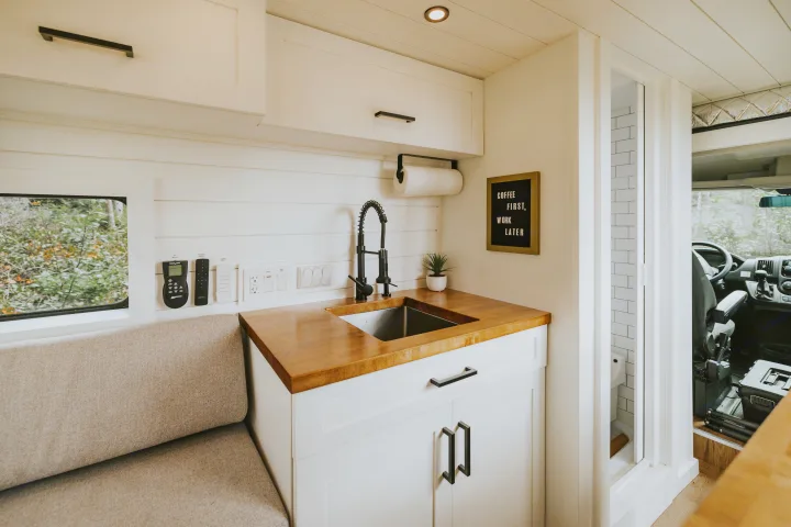 Experience compact comfort in this modern RV rental's kitchen and living area, featuring a cozy bench and full amenities.. Ram Promaster 2500 2019