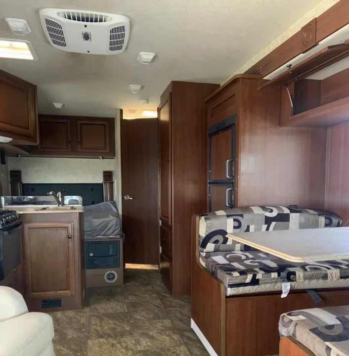 This RV rental interior features a functional kitchen, dining booth, and bedroom section, all in warm wood tones and neutral colors.. Jamboree Searcher 2013