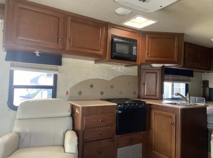 RV rental interior: kitchen with wood cabinets, microwave, stove, sink, and a cream recliner. Ready for adventure!. Jamboree Searcher 2013