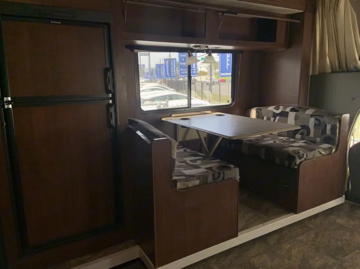 Step into this rv rental's built-in dinette, ideal for meals & games. Refrigerator to the left, window view of a dealership.. Jamboree Searcher 2013