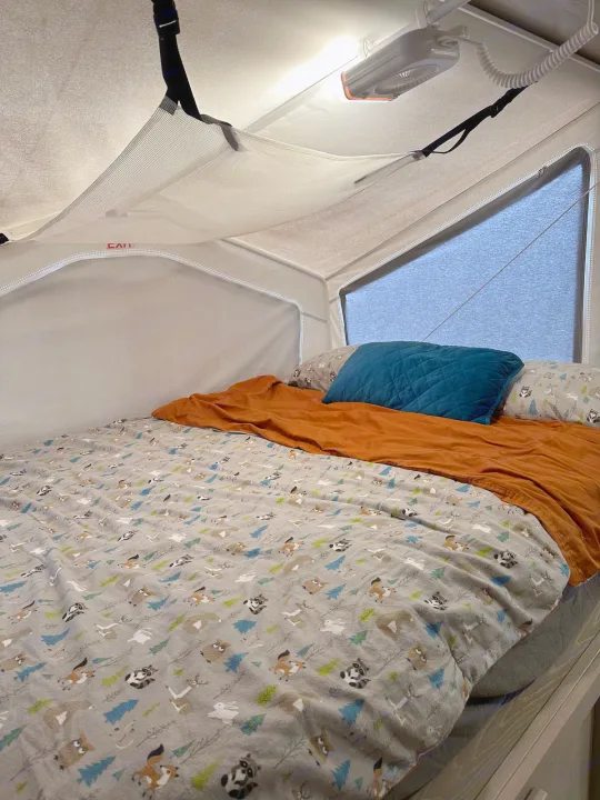 Cozy RV rental bed with forest animal comforter, fan, & storage net in a compact sleeping area.. Forest River Flagstaff Shamrock 2022