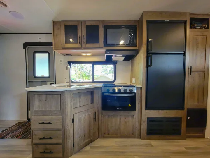 Spacious RV rental kitchen with modern amenities: full fridge, microwave, oven, sink, and ample wood cabinetry.. Heartland RVs Pioneer 2021