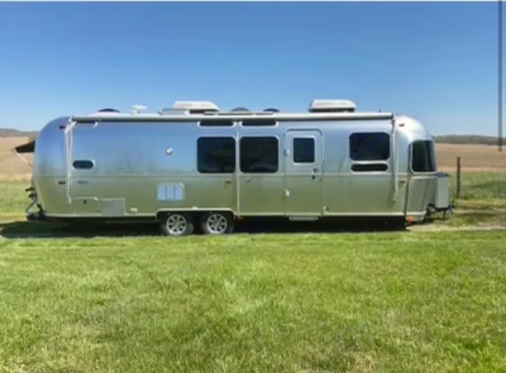 Sleek silver Airstream travel trailer for RV rental, parked in a bright green field under a clear blue sky.. Airstream Flying Cloud 2019