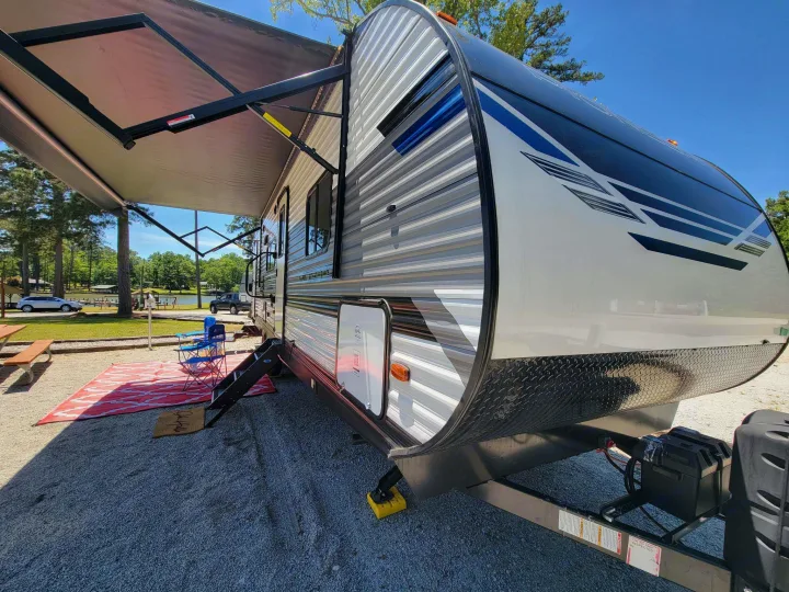 Scenic rv rental setup: A modern travel trailer with an extended awning and outdoor seating at a beautiful lakeside campsite.. Heartland RVs Pioneer 2021