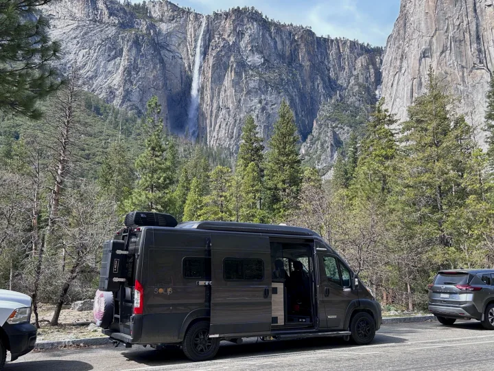 An rv rental, a Winnebago Solis camper van, parked in front of towering Yosemite Falls and granite cliffs. Perfect nature travel.. Winnebago Solis 2022