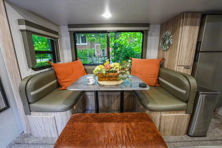 Discover a cozy RV rental dinette: olive green booth, orange pillows, table with flowers, and large nature views.. Winnebago Minnie 2022
