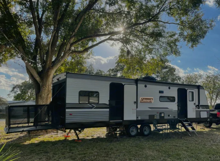 This Coleman RV rental offers a spacious outdoor camping setup with a deck, chairs, and shade under a large tree.. Coleman Other 2022