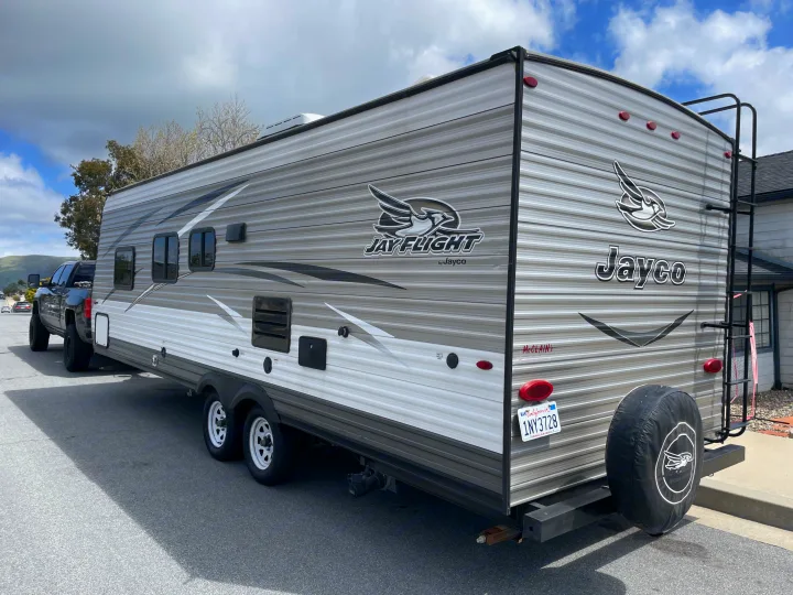 A grey & white Jayco travel trailer, perfect for an rv rental adventure, hitched to a truck on a partly cloudy day.. Jayco Jaycoflight 2017