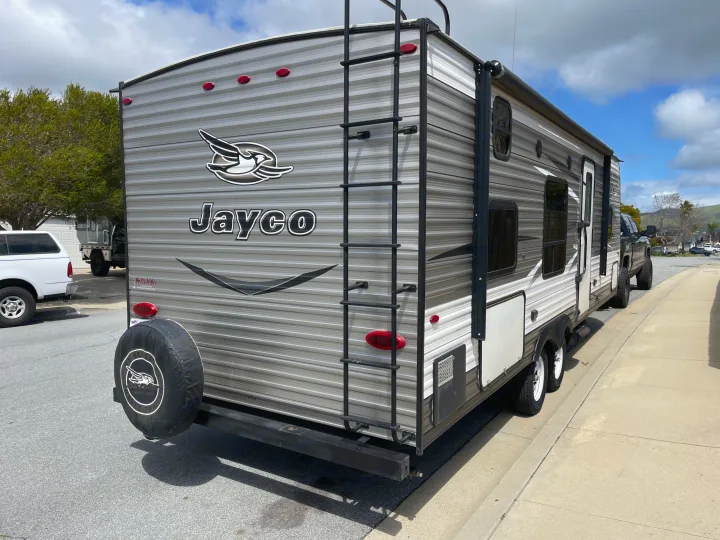 A striped Jayco RV, perfect for an rv rental, parked curbside. Features a rear ladder, spare tire, and windows along the side.. Jayco Jaycoflight 2017