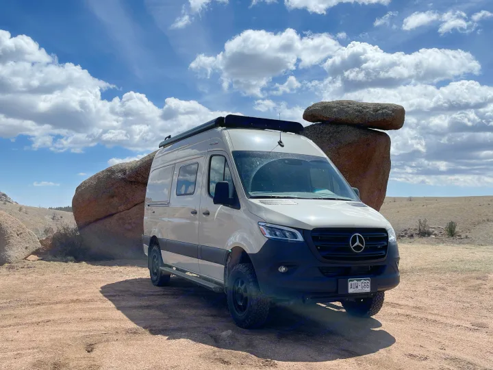 Adventure awaits! This off-road Mercedes Sprinter RV rental is parked by large rocks under a blue sky.. Winnebago Revel 2022