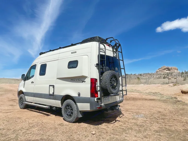 An off-road Winnebago Revel camper van, ideal for RV rental adventures, parked on a dirt trail with rocky hills under a blue sky.. Winnebago Revel 2022