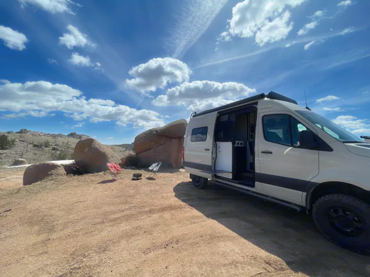 This RV rental is parked among large rocks with camp chairs & fire pit nearby, perfect for a scenic outdoor adventure.. Winnebago Revel 2022