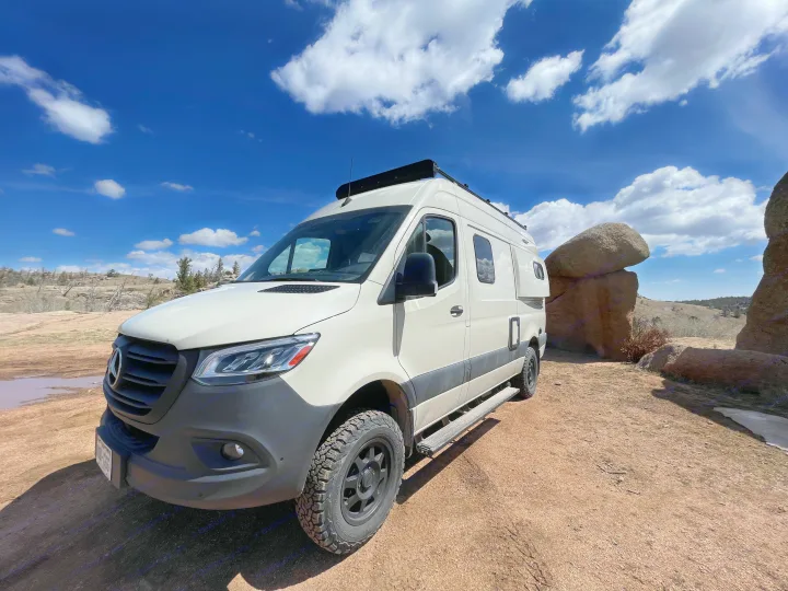White Mercedes Sprinter camper van (RV rental) parked on a dirt trail under a blue sky with unique rock formations.. Winnebago Revel 2022