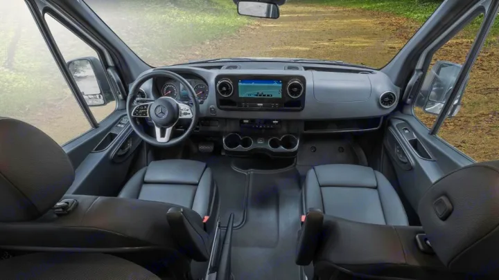 View from the back of a Mercedes-Benz van interior, perfect for RV rental. Shows dashboard, steering wheel, and front seats.. Winnebago Revel 2022