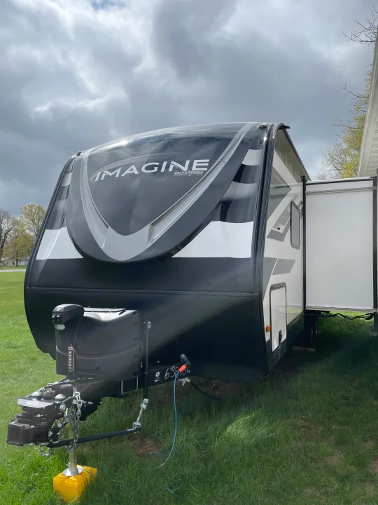 Black and white travel trailer RV rental parked on grass with its side room extended, ready for your outdoor adventure.. Grand Design Imagine 2022