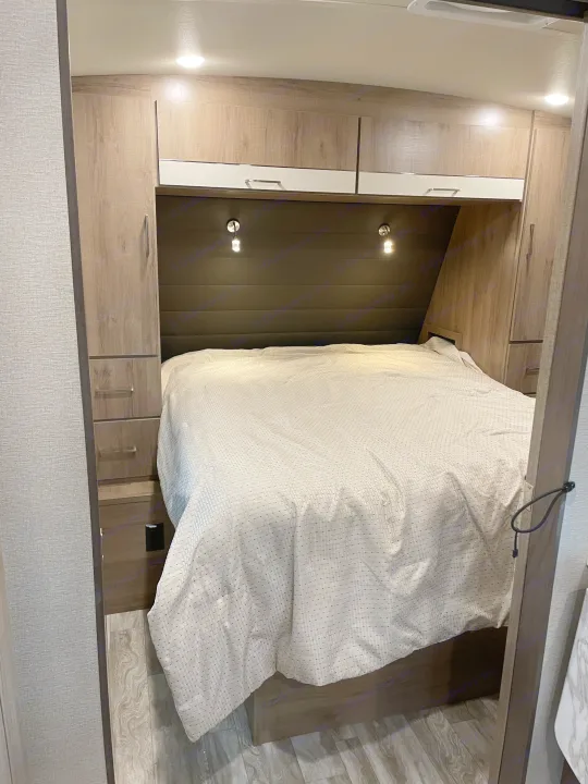 Spacious RV rental bedroom featuring a queen bed, reading lights, and built-in wood-look cabinetry.. Grand Design Imagine 2022
