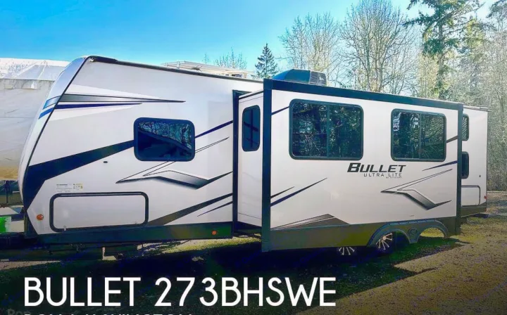Modern white Bullet Ultra Lite travel trailer (RV rental), model 273BHSWE, with slide-out extended in an outdoor setting.. Keystone RV Bullet Ultra Lite 2021