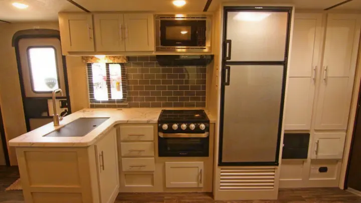 Compact rv rental kitchen: light cabinets, tiled backsplash, stove, microwave, fridge, and a sink.. Keystone RV Bullet Ultra Lite 2021