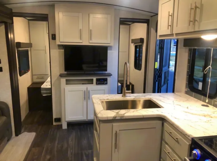 RV rental interior featuring a kitchen with a sink, marble-look counters, entertainment center, and bedroom access.. Keystone RV Bullet Ultra Lite 2021